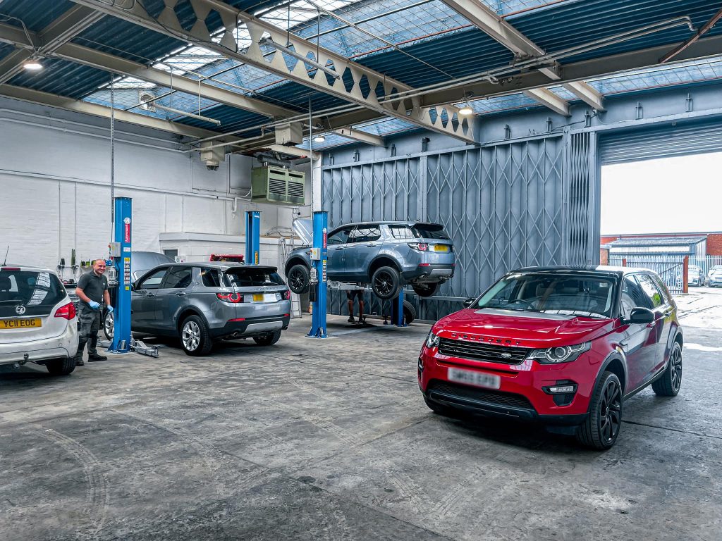 A red Land Rover discovery is parked in the ASM Independent garage. There is also a white Vauxhall and two silver Land Rovers up on the jacks. ASM Independent: Independent Jaguar and Land Rover Specialists Wakefield.