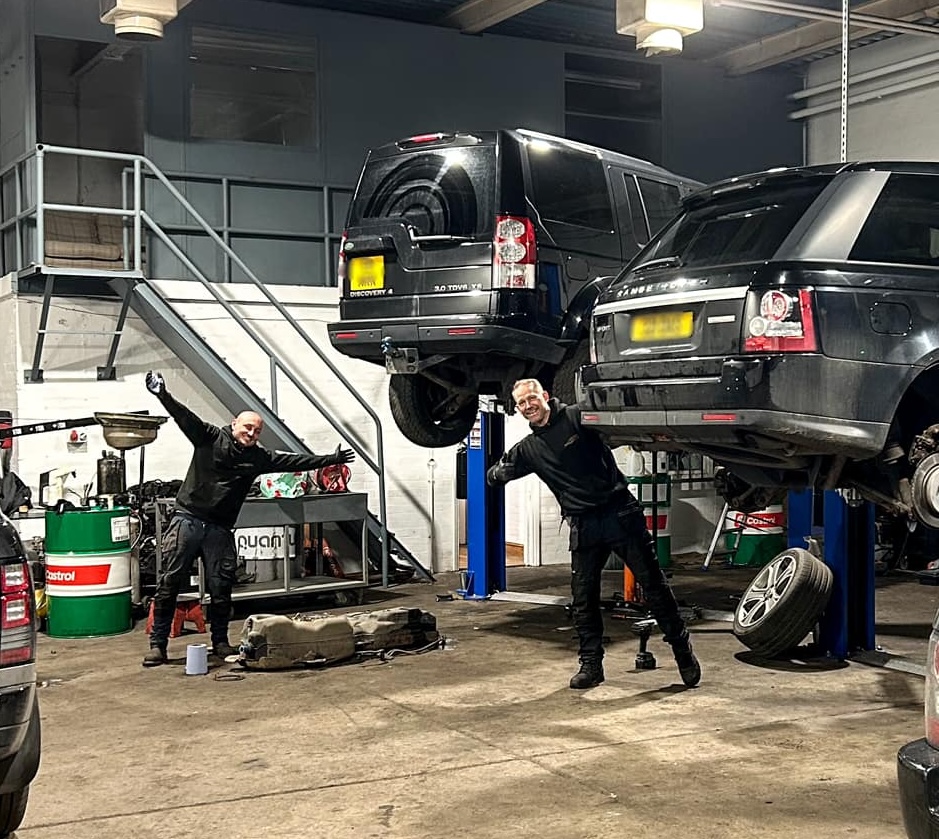Andy and Sam of ASM Independent are posing in a playful way for the cameras while working. There are one black Range Rovers and one Land Rover on ramps behind them in the ASM Independent garage. ASM Independent: Independent Jaguar and Land Rover Specialists Wakefield.